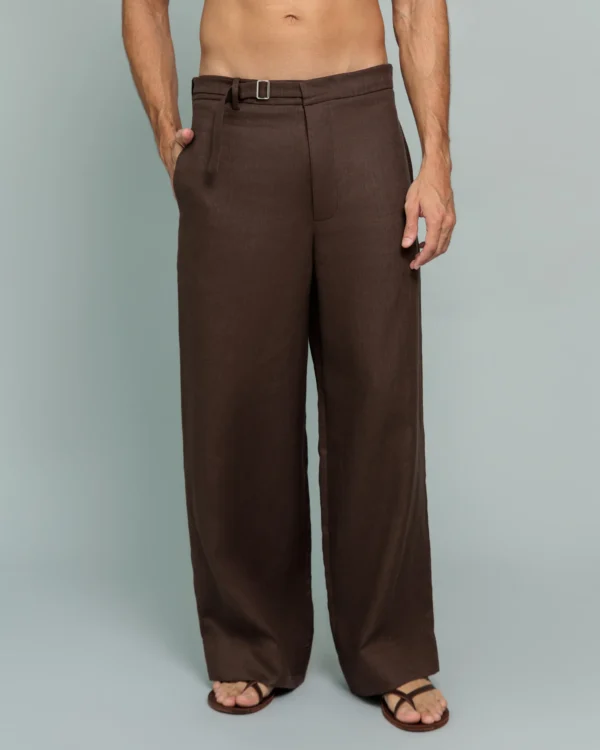 Man wearing 20Two Elemental's GHAF rooted trouser in brown, wide-leg silhouette with a self-tie belted waist, shirtless, standing against a soft sage studio backdrop