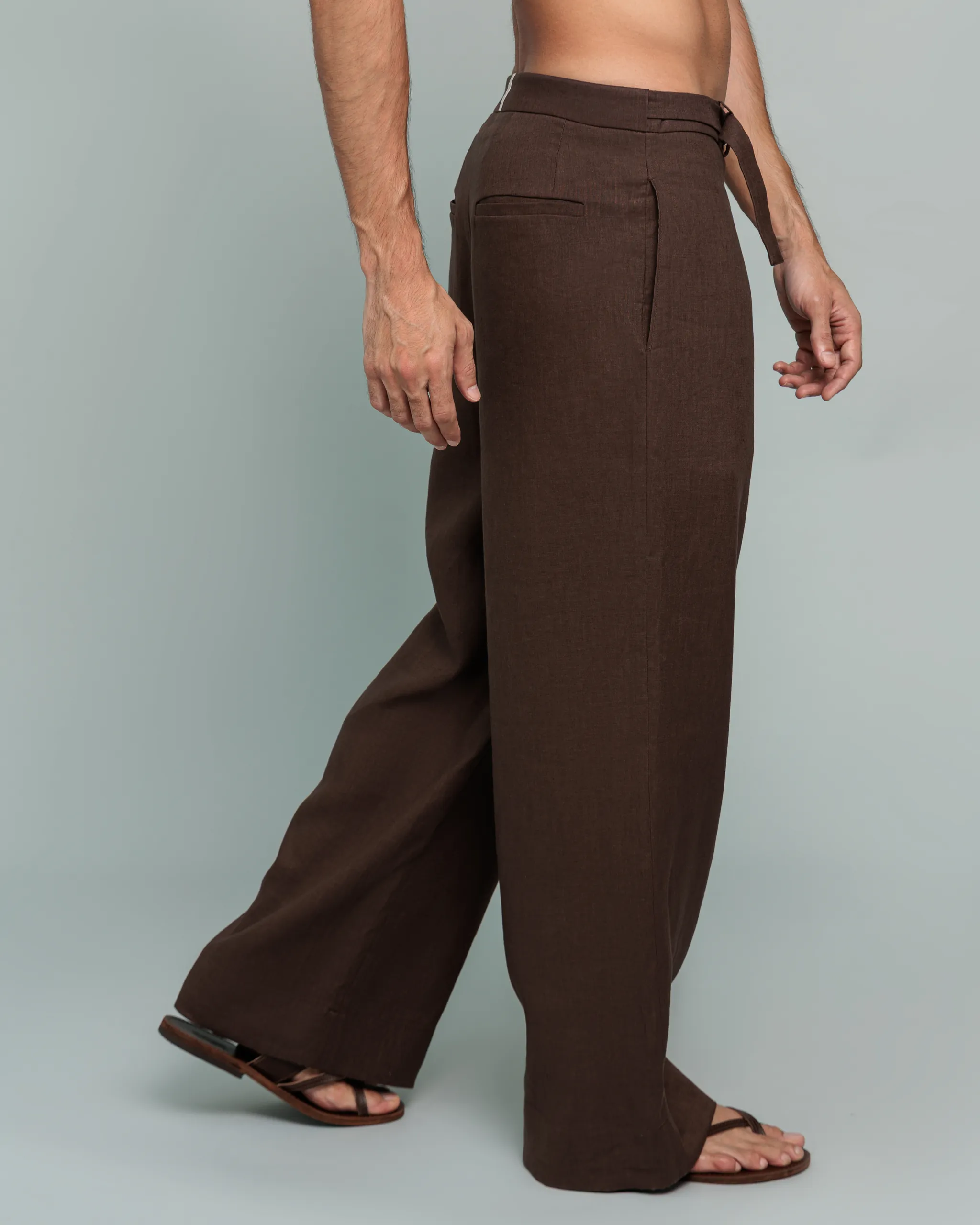 Side view of a man walking in 20Two Elemental's GHAF rooted trouser in brown, wide-leg silhouette with sandals