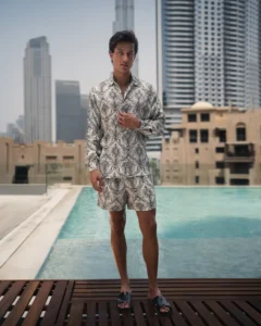 Man wearing a refined and styled patterned lotus plant fiber shirt and matching shorts from 20Two Elemental, standing by a pool with a modern city skyline in the background, front view
