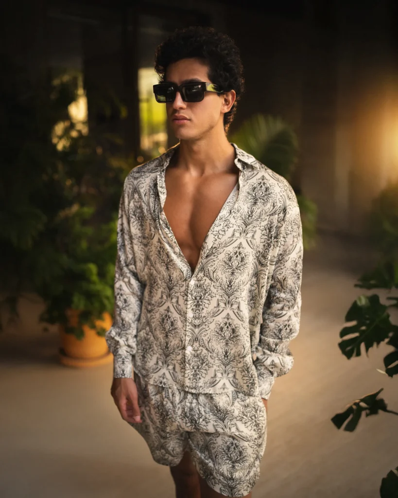 Man wearing a modern long-sleeve lotus plant fiber shirt from 20Two Elemental with a black-and-white botanical pattern, styled partially unbuttoned with bold dark rectangular sunglasses