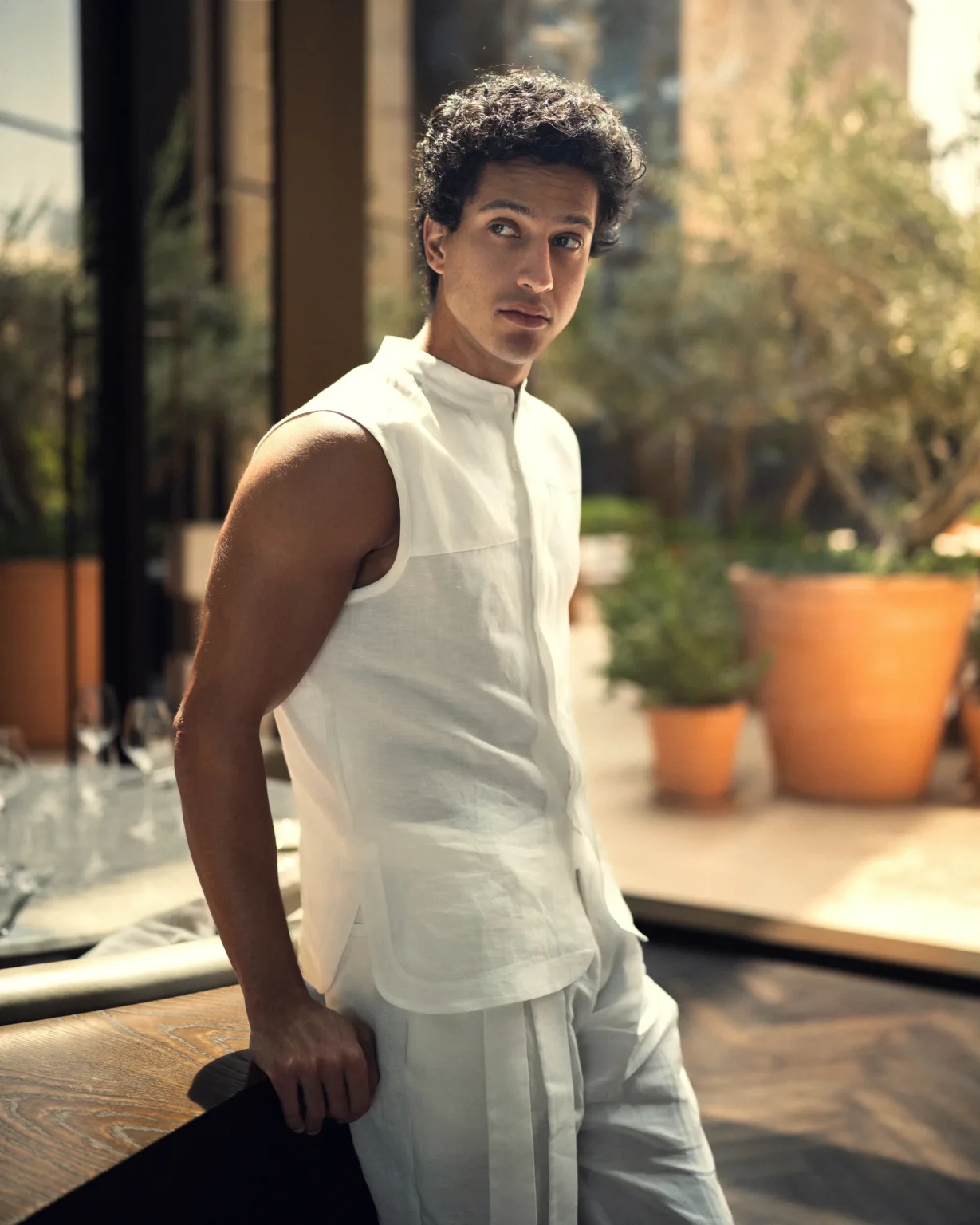 Man wearing a contemporary natural white, sleeveless shirt with mandarin collar and curved side hems from 20Two Elemental, calm and stylish sunlight atmosphere